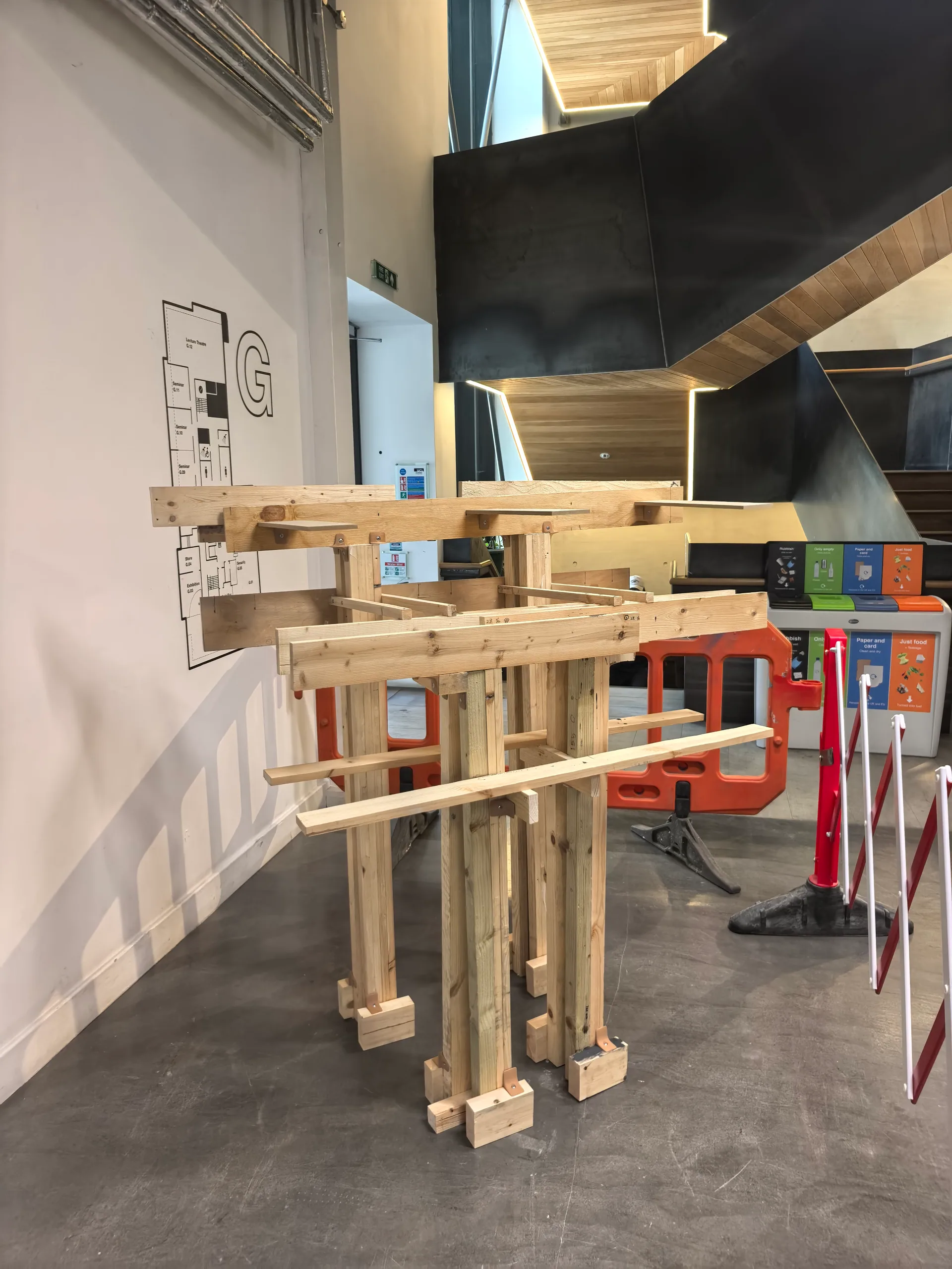The Bartlett Autumn Show 2026: Khora 3 Canopy: a shelter frame of posts and layered beams, standing by the stair on the ground floor